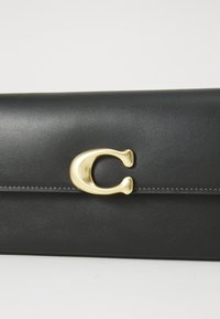 Portefeuille en cuir noir avec un fermoir métallique doré en forme de lettre "C" et des coutures visibles le long du bord du rabat.