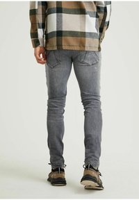 Grå slim-fit jeans med en blekt struktur, ihop med en brun och beige rutiga skjorta. Svarta och bruna sneakers fulländar looken.
