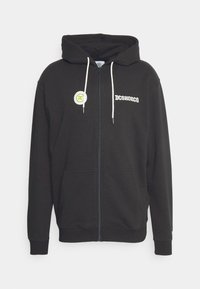 Schwarze Zip-Hoodie aus weicher Baumwolle, mit Kängurutasche, Kapuze mit Kordelzug und bedruckten Logo-Akzenten in Weiß und Grün.