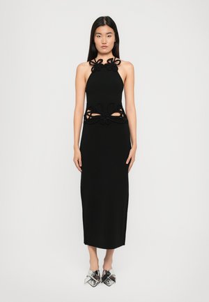 Vestido negro de cuello halter con lazos decorativos en el escote y cortes en la cintura. Textura suave, silueta ajustada, diseño hasta la rodilla, combinado con zapatos metálicos.