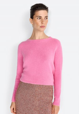 Pull en tricot rose et moelleux avec un col rond et des manches longues ; associé à une jupe à carreaux marron en tissu texturé.