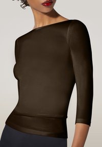 Frau in einem enganliegenden, dunkelbraunen Longsleeve-Oberteil mit Bootschnitt, roten Lippenstift und lockigem Haar, das nach hinten gebunden ist.