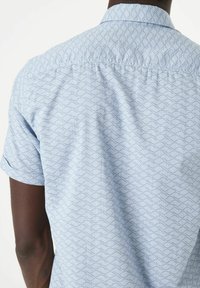 Korte mouwen overhemd in lichtblauwe stof met een golfpatroon. Heeft een button-down kraag, zachte textuur en een relaxte pasvorm.