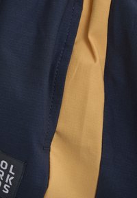 Marineblauwe en gele sportshorts met een gestructureerde stof, opvallende zijpaneel en een merkpatch met witte letters.