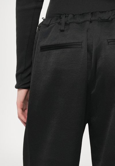 Černé kalhoty vyrobené z měkké tkaniny se nařaseným elastickým pasem. Dvě zadní kapsy s elegantními černými akcenty. Jednoduchý, elegantní design.
