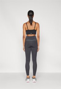 Sujetador deportivo negro con tirantes ajustables y tela texturizada, combinado con leggings negros de cintura alta con costuras decorativas y corte hasta el tobillo.