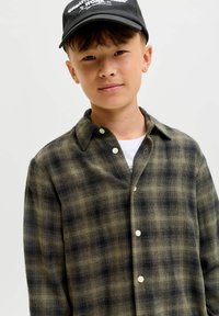 Grønternet flannel skjorte med en afslappet pasform, krave og perleagtige knapper. Båret over en hvid T-shirt, suppleres af en sort kasket.