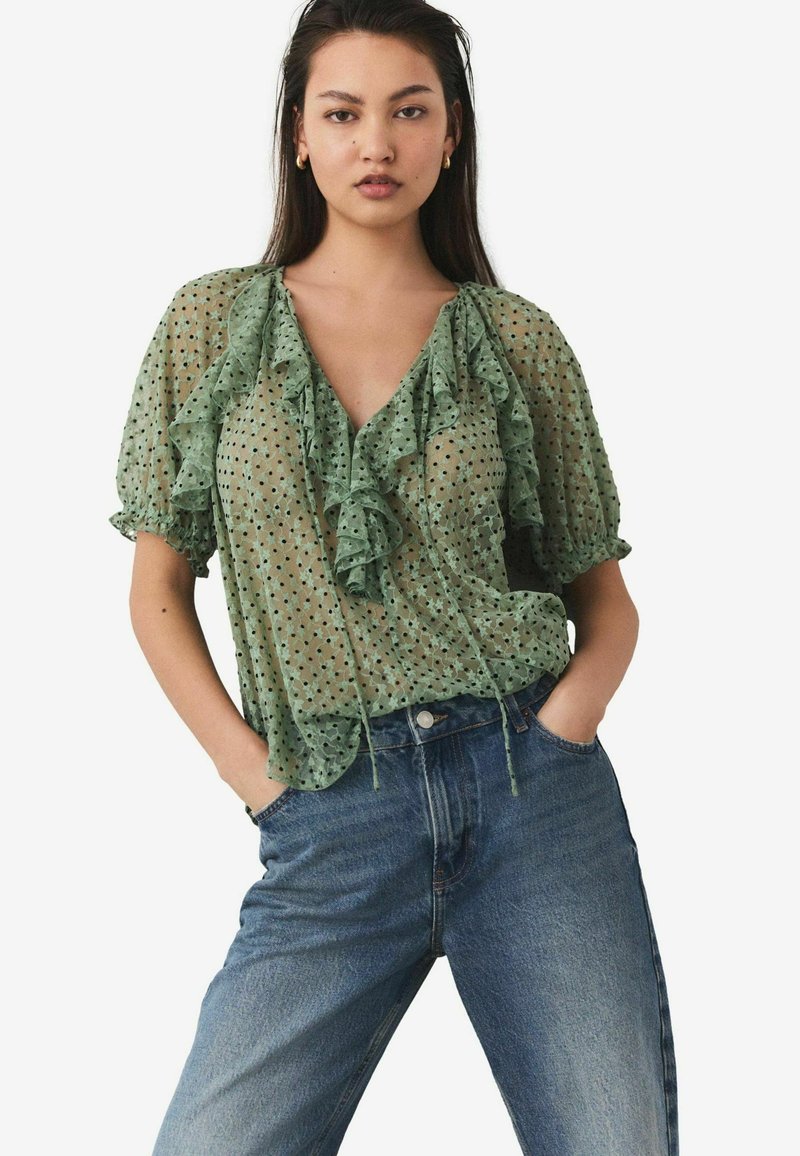 Groene doorschijnende blouse met stippen, met een ruffles halslijn en mouwen, gecombineerd met blauwe high-waisted jeans. Gelaagde stof, casual pasvorm.
