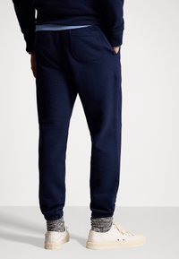 Pantaloni della tuta blu navy realizzati in un tessuto morbido, con gamba affusolata, polsini a costine e una tasca posteriore, abbinati a sneaker beige chiaro.