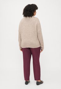 Beige pletený svetr s volným střihem, doplněný burgundskými kalhotami. Černé boty se cvočky, z pohledu zezadu.