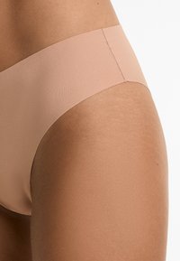 Beige naadloze hipsterondergoed met een zachte textuur, elastische tailleband en minimale stikdetails. Ontworpen voor comfort en discretie.
