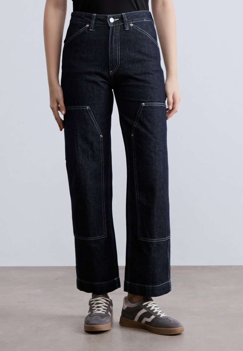 Σκούρο τζιν παντελόνι με φαρδιά πόδια και ανοιχτόχρωμες ραφές αντίθεσης, με μπροστινές τσέπες και κούμπωμα με κουμπί στη μέση.