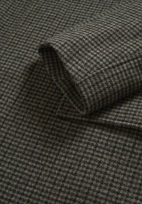 Tessuto di lana in una fantasia a quadri marrone e grigio, con una texture morbida e un angolo piegato che mette in evidenza il dettaglio del design.