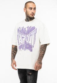 Creme oversized t-shirt med et lilla grafisk print, der står "TAPOUT." Har korte ærmer og en løs pasform. Bæres sammen med slidte sorte jeans.