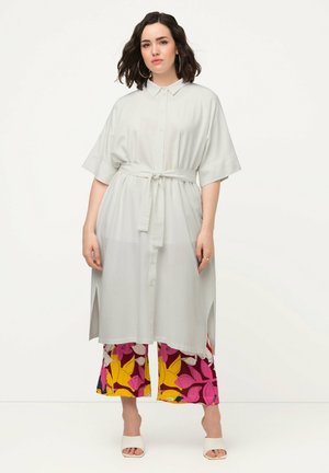 Helles graues, kurzärmliges Hemdkleid mit tailliertem Bund und seitlichen Schlitzen. Kombiniert mit bunten, gemusterten weitbeinigen Hosen.