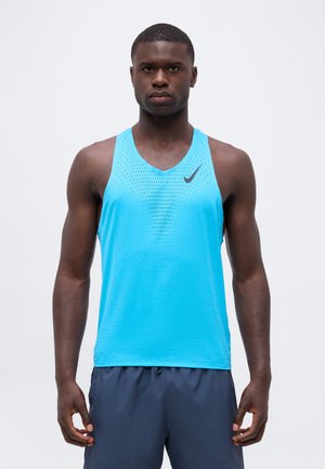 Atletisk mand vendt fremad iført en blå ærmeløs sportstrøje med sort Nike-logo og mørkeblå shorts mod en ensfarvet baggrund.