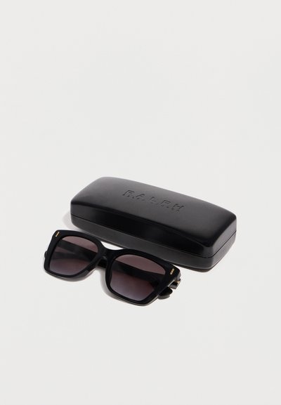 Μεγάλα τετράγωνα μαύρα γυαλιά ηλίου με σκουρόχρωμους φακούς, τοποθετημένα δίπλα σε μια σκληρή θήκη με το λογότυπο Ralph Lauren σε μαύρο, πάνω σε λευκή επιφάνεια.