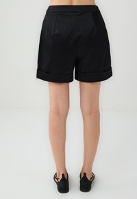 Pantaloni corti neri su misura con una texture liscia, caratterizzati da orli risvoltati. La vita si adatta bene alla vita con pieghe sottili.