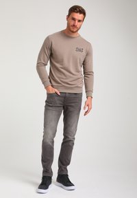 Gray sweatshirt with a round neck and embroidered design on the chest, paired with faded gray jeans and black high-top sneakers.