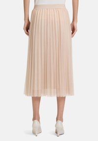 Gonna midi plissettata rosa chiaro realizzata in tessuto morbido, con una vita ampia e una silhouette fluida. Indossata con scarpe con tacco alte beige.