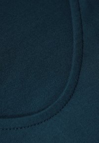 Teal stof met een gladde textuur, voorzien van een gebogen naaddetail. Close-upweergave benadrukt de stiksels langs de randen.