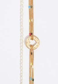Pulsera de múltiples hilos en oro con un charm en forma de corazón con texto grabado, acompañada de una fila de perlas blancas brillantes. Acentos decorativos coloridos salpican las cadenas.
