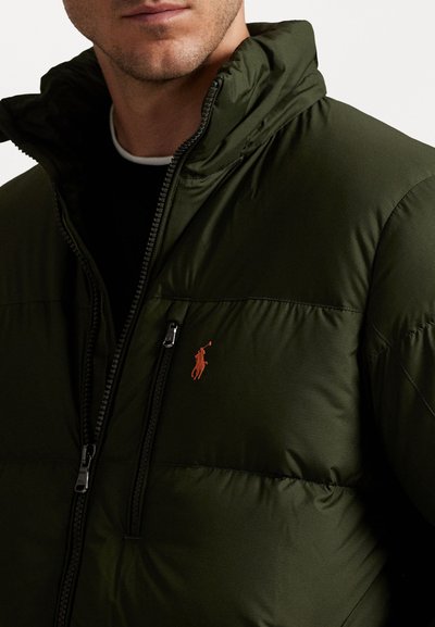 Mørkegrøn pufferjakke med høj krave, lynlås foran og et orange polo-logo på brystet. Har en glat, blank stofstruktur.