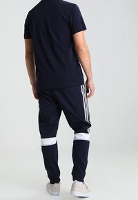 Námořnická modrá tričko s krátkým rukávem a kulatým výstřihem, spárované s námořnickými tepláky s bílými pruhy a akcenty na dolních nohách.