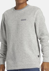Grauer Sweatshirt mit strukturiertem Finish, Rundhalsausschnitt und gerippten Bündchen. Verfügt über ein kleines Logo-Patch auf der Brust und ein Etikett am Saum.