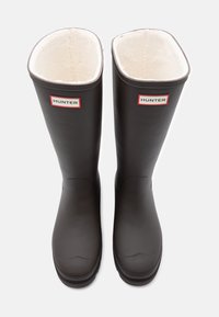 Hnedé gumové dažďové čižmy s fleecovou podšívkou, so štvorcovým strihom na vrchu, textúrovanou podrážkou a červenobielymi logovými akcentmi.