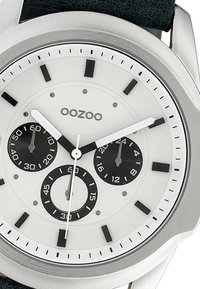 Montre en acier inoxydable argenté avec un cadran blanc, des sous-cadrans noirs et des index noirs. Dotée d'un bracelet en cuir noir et d'aiguilles blanches.