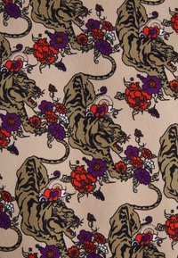 Tissu beige à motifs répétitifs de tigres féroces entourés de motifs floraux rouges, violets et blancs.