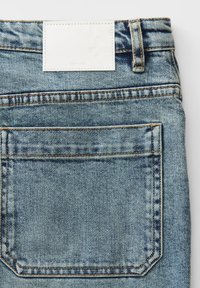 Vue arrière d'un jean en denim bleu clair montrant une grande poche arrière, des passants de ceinture et une étiquette blanche rectangulaire vide au-dessus de la poche.