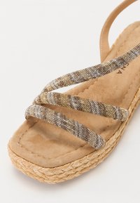 Sandalo platform in tessuto intrecciato marrone, con molteplici strisce scintillanti, dotato di una morbida soletta in suede e una suola in juta intrecciata.