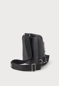 Černá syntetická crossbody taška s obdélníkovým tvarem, zipovým uzávěrem, nastavitelným popruhem a texturovaným povrchem. Obsahuje stříbrné kovové prvky.