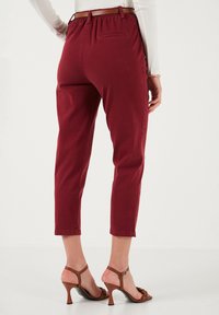 Pantaloni cropped in cotone rosso con vita elasticizzata e un sottile dettaglio della tasca posteriore, abbinati a tacchi strappy marroni.
