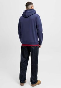 Marinebl�å hættebluse med en afslappet pasform, der har en kangaropocket. Parret med mørk denim jeans og tan-farvet fodtøj.