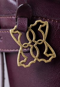 Maroon leather bag featuring a decorative gold-toned metal accent. The accent has an intricate cut-out design, enhancing the bag's style.