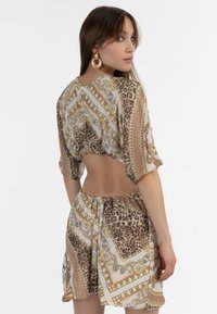 Leopardenmuster-Crop-Top mit goldenen dekorativen Mustern, kurzen Ärmeln und passendem Rock. Der Stoff hat eine glatte Textur und helle Farben.
