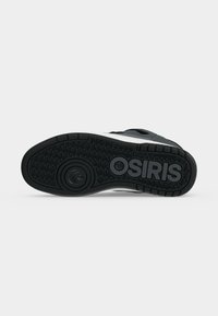Σόλα από ένα ασπρόμαυρο sneaker Osiris με υφή πρόσφυσης και κυκλικό σχέδιο πέλματος σε απλό γκρι φόντο.
