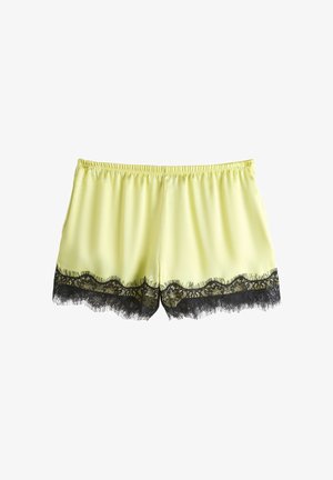 Pantalones cortos de seda amarillo claro con adornos de encaje floral negro en los dobladillos y cintura elástica, mostrados sobre un fondo blanco.