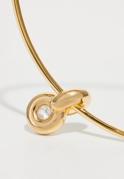 Goldring mit einem gedrehten Design, das einen runden Anhänger mit einem klaren, facettierten Edelstein auf einem weißen Hintergrund zeigt.