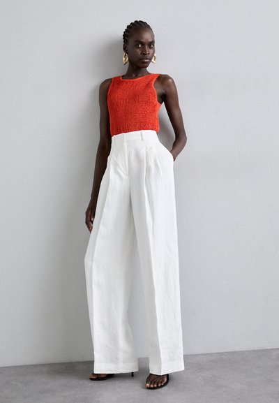 Κόκκινο πλεκτό αμάνικο τοπ με υφή και λευκά παντελόνια με ψηλή μέση και φαρδιά πόδια. Μαύρες λουστρίνι γόβες και χρυσά κρίκοι σκουλαρίκια.