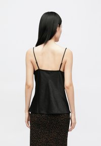 Zwarte camisol met dunne verstelbare bandjes, voorzien van een gestructureerde stof en een uitlopende zoom. Gecombineerd met een bruin, gevlekt rokje.