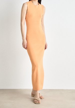 Robe ajustée sans manches en tissu orange doux, avec un col rond et un ourlet évasé. Associée à des sandales de couleur claire.