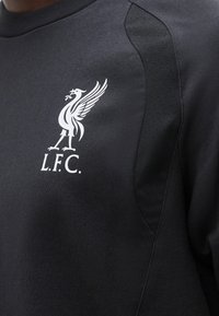 Μαύρη φούτερ με άσπλο λογότυπο της Liverpool Football Club που απεικονίζει ένα πουλί Liver που κρατά κλαδί, ορατό στην περιοχή του στήθους.