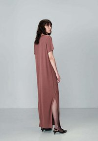 Abito lungo in rosa polveroso, realizzato in un tessuto morbido con maniche corte, spacchi laterali e una vestibilità rilassata, abbinato a scarpe nere a punta.