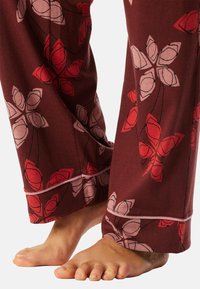 Pantalones de pijama burdeos con un patrón floral que presenta pétalos rojos y rosas contorneados en negro. El material es suave y tiene un ajuste cómodo.