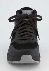 Zwarte sportieve schoen van mesh en synthetische materialen, met een ronde neus, vlakke grijze rubberen zool en donkerbruine veters.