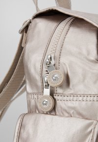 Borsa a tracolla beige chiaro con una texture liscia e lucida, dotata di cerniere argento e dettagli del logo arrotondati sui tirazip.